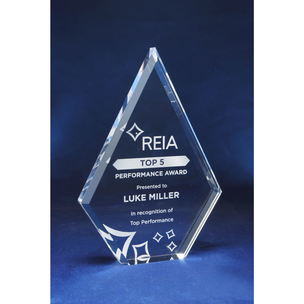 A diamond-shaped acrylic trophy with a clear finish and a blue background. Features engraving and a logo.