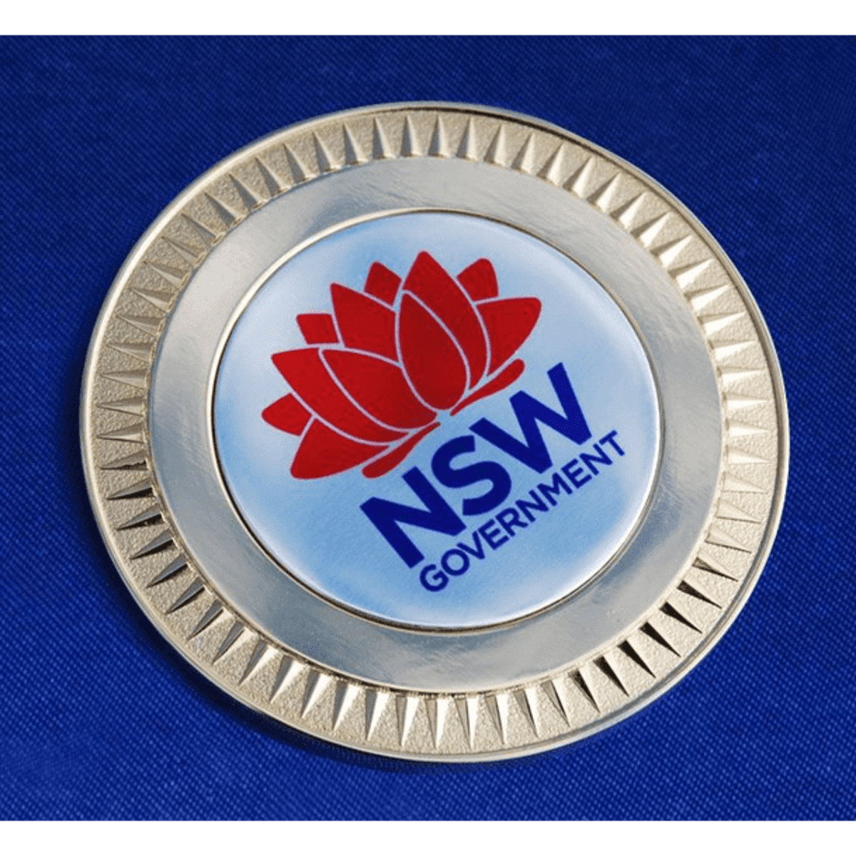 A 70mm medallion featuring a logo, set against a blue velvet background.