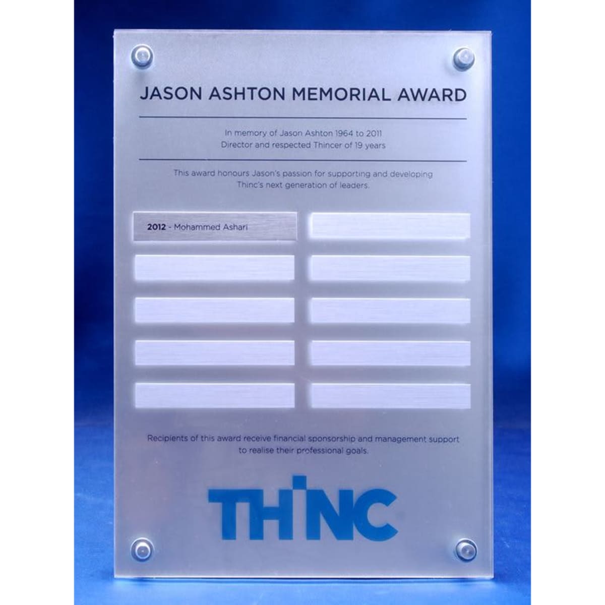 A clear acrylic award plaque with engraved sections for names, featuring a blue logo at the bottom.