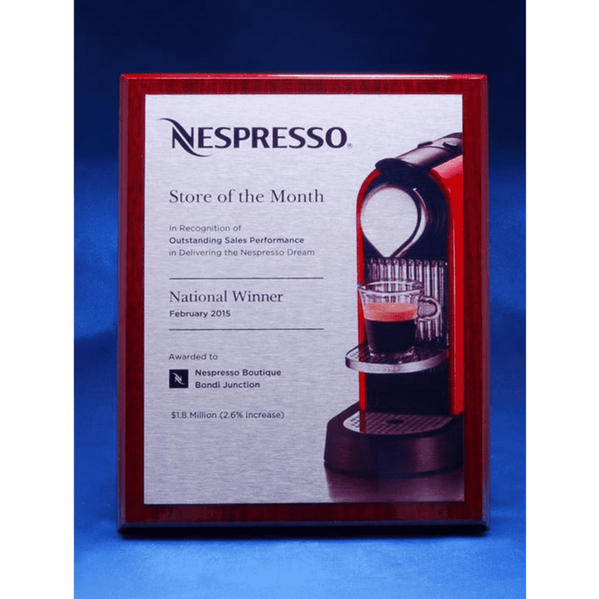 A printed plate mounted on a polished timber plaque featuring a coffee machine design and a logo.