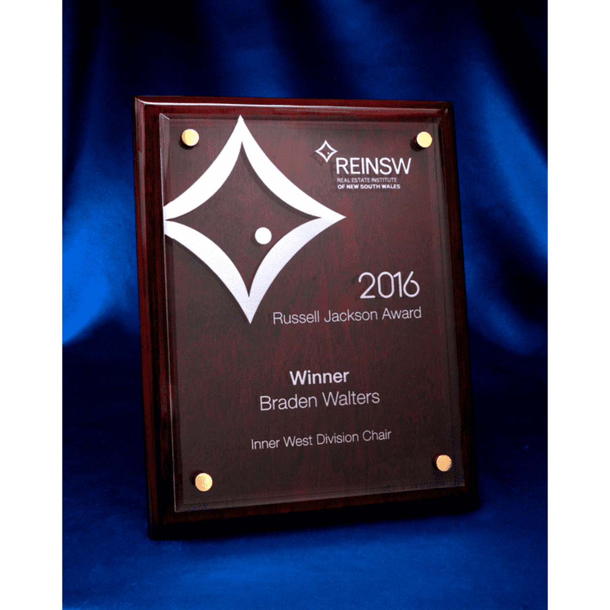 A rosewood plaque featuring a laser-engraved acrylic panel, displaying an award design. It has a glossy finish and gold accents.