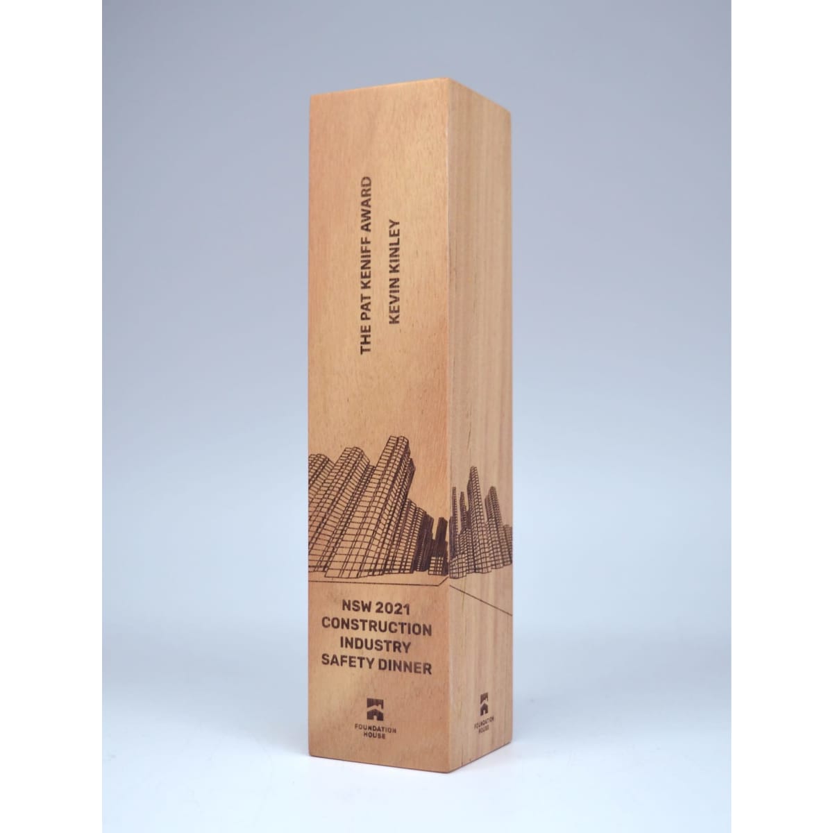 A wooden trophy in a warm wood tone with a decorative skyline design and a branded logo.