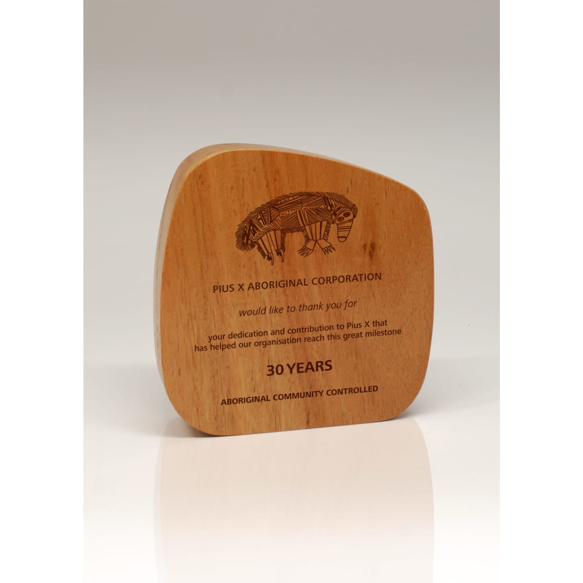 A wooden trophy with a curved shape, featuring an engraved design and text celebrating 30 years of achievement.