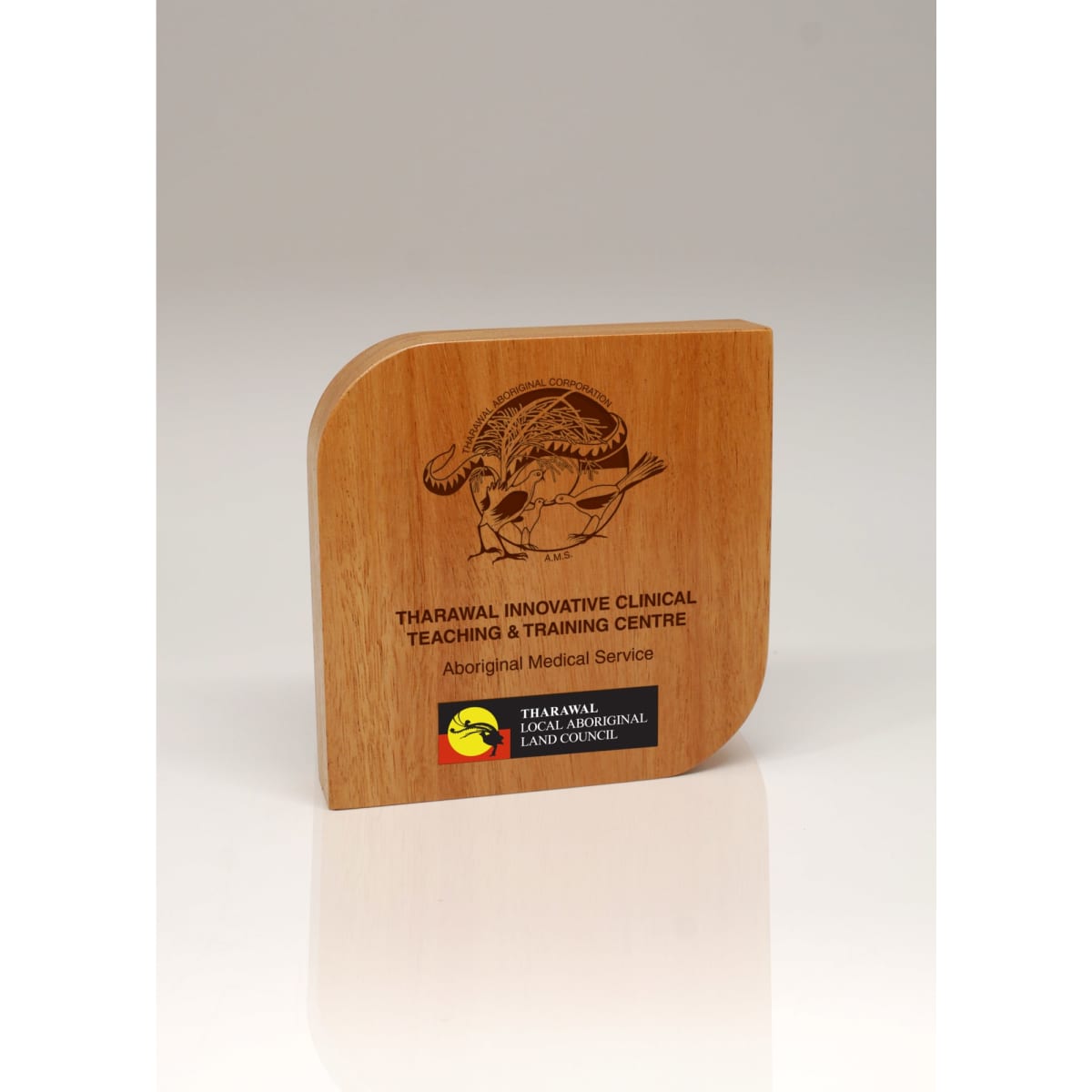 A wooden trophy with a curved edge, featuring a design and a logo. The colour is a light brown wood finish.