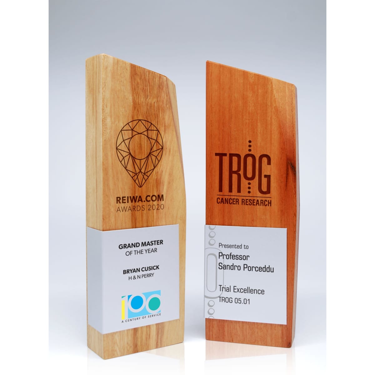 A wooden trophy with a sleek design, showcasing natural grain in light brown, featuring a logo and engraved text.