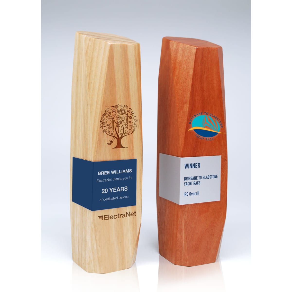 Two wooden trophies made of light and dark timber with engraved designs and metal wraps, showcasing a winner's title.