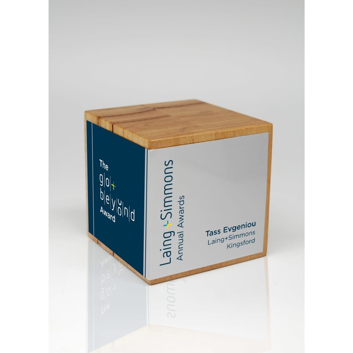 A wooden cube trophy in natural wood colour with a metallic silver and blue panel, featuring a logo.