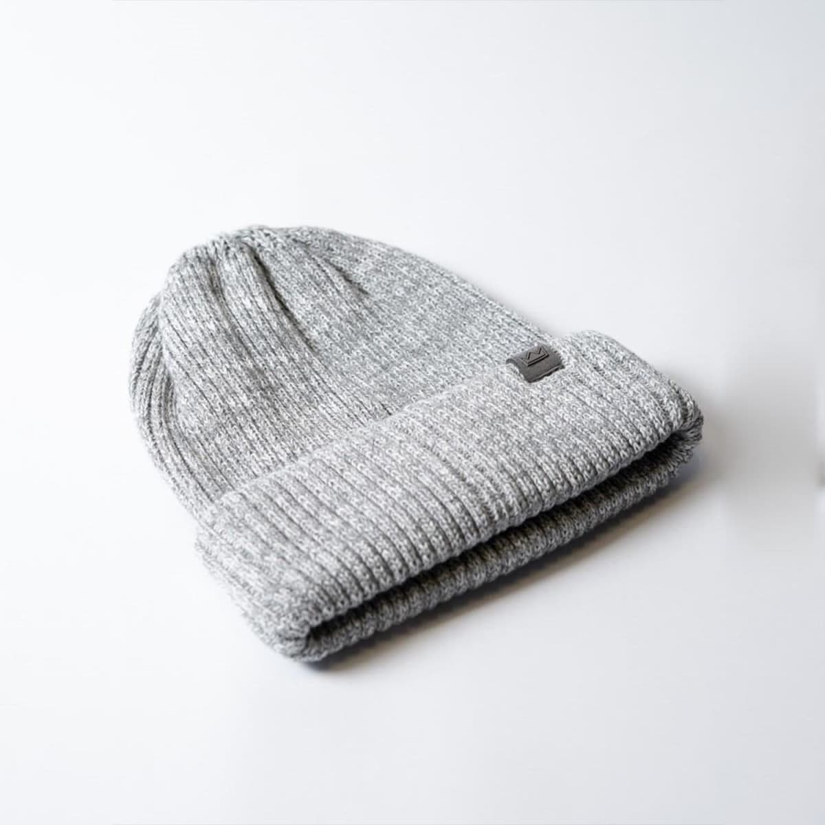 A grey knitted beanie with a cuff and a logo, designed for warmth and style.