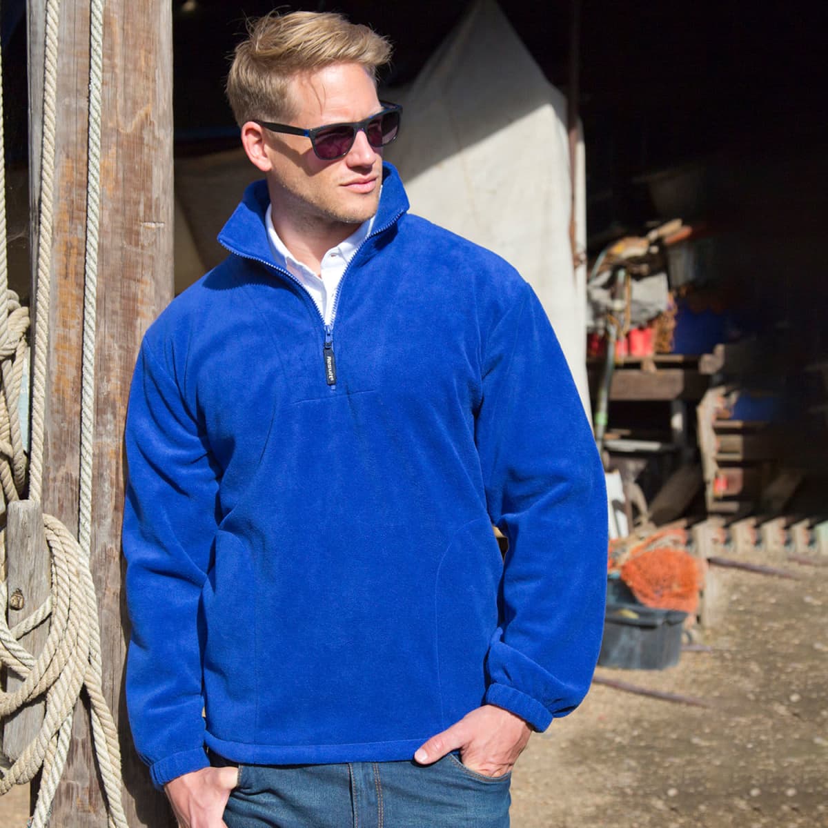 A blue fleece quarter-zip jumper with a collar and an embroidered logo, worn by a man in sunglasses.