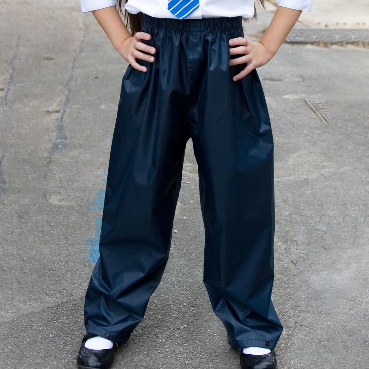 Youth rain trousers in black, featuring an elastic waist and a loose fit. Suitable for outdoor activities.