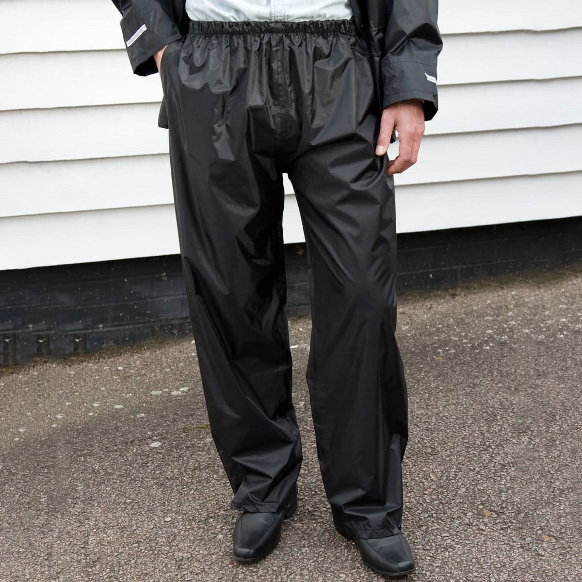 Black adult rain trousers feature an elasticised waistband and cuffs, with a logo on the outer side.