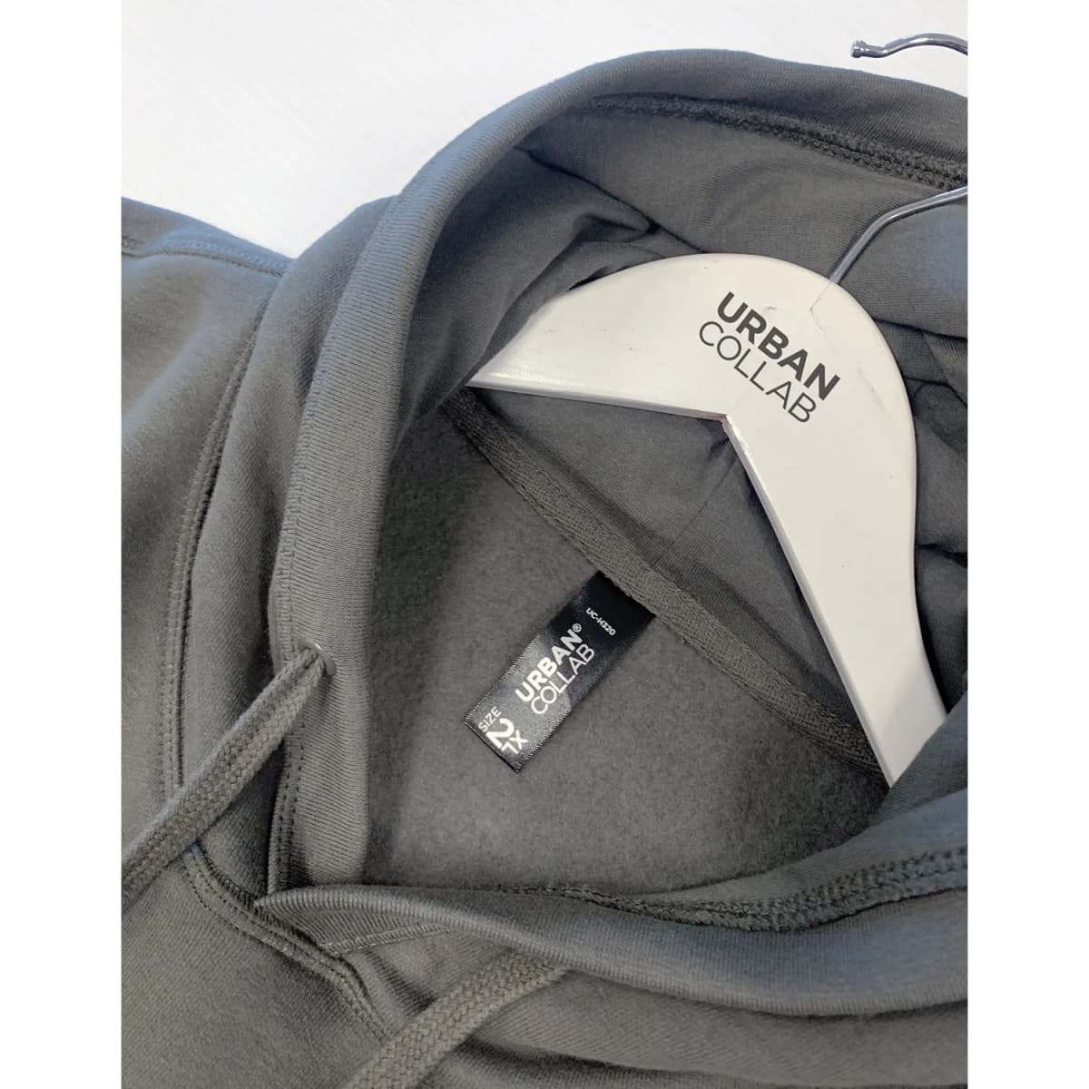 A grey hoodie featuring a hood and a label with branding, hanging on a clothes hanger.