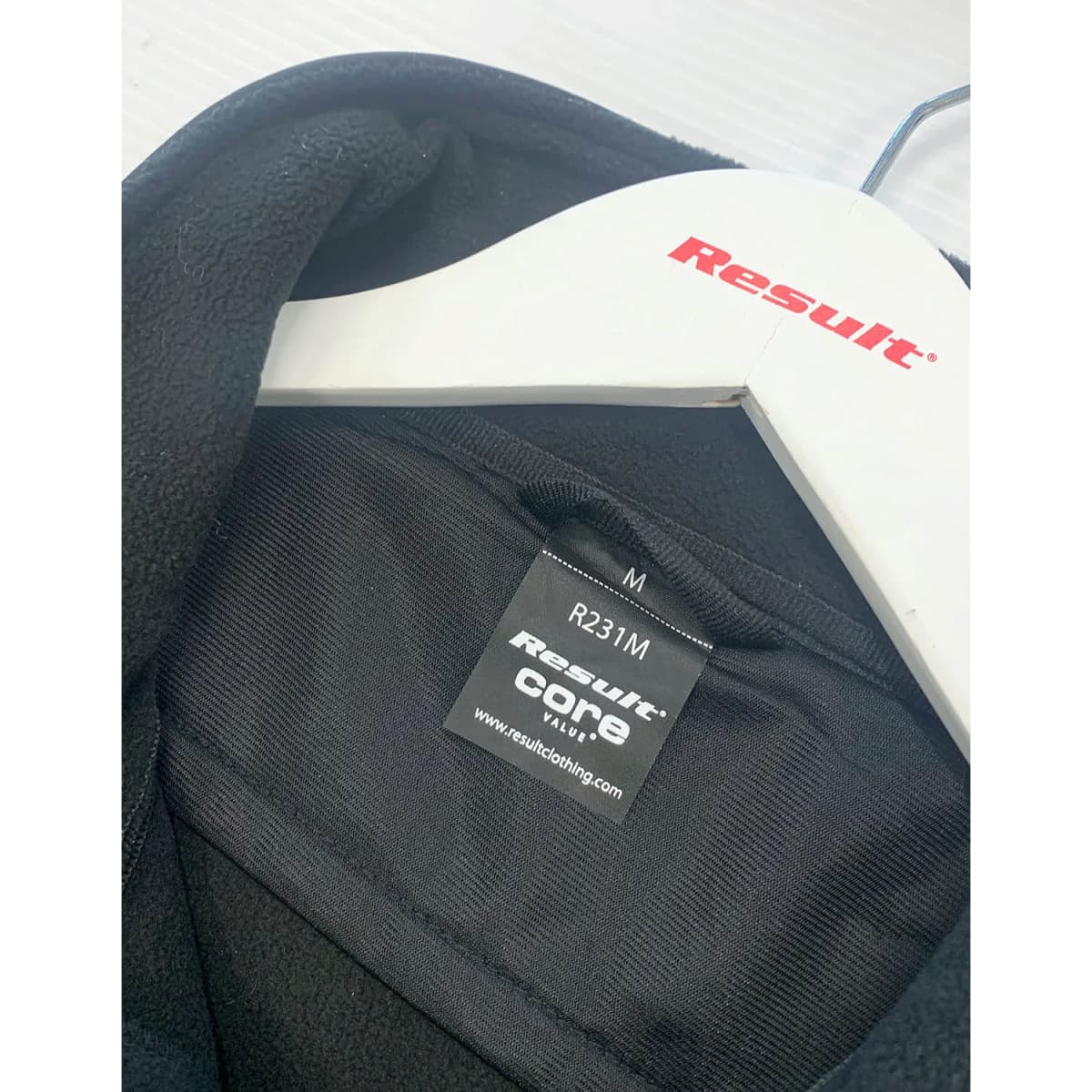 A black jacket with a label featuring a logo, hanging on a white hanger.