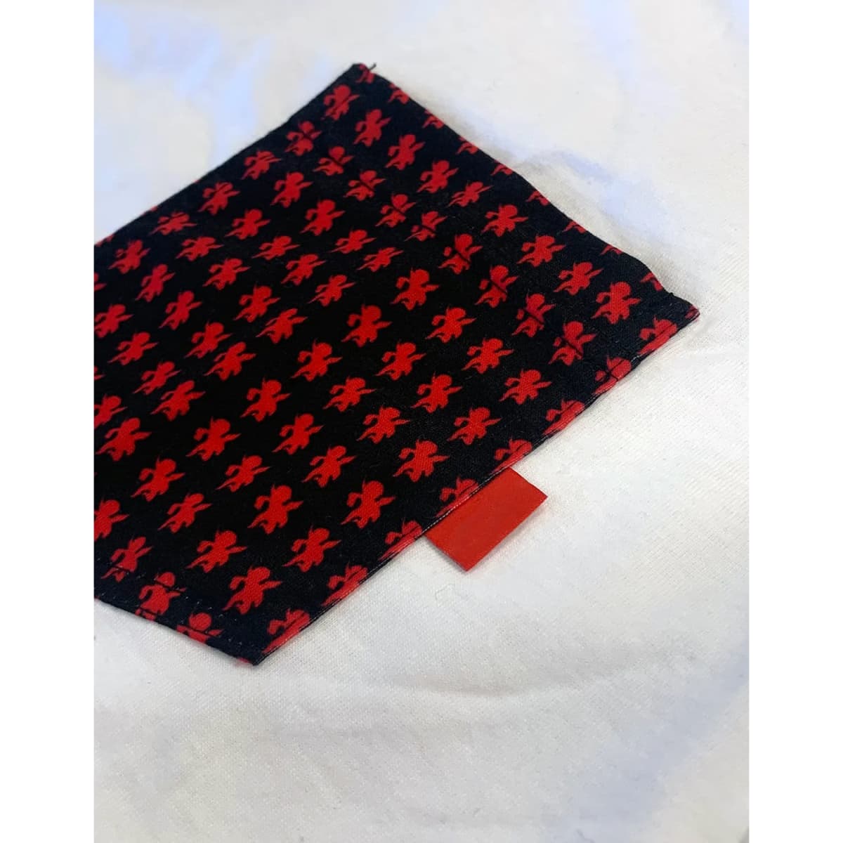 A patterned fabric swatch featuring red designs on a black background, with a small red tag at the edge.