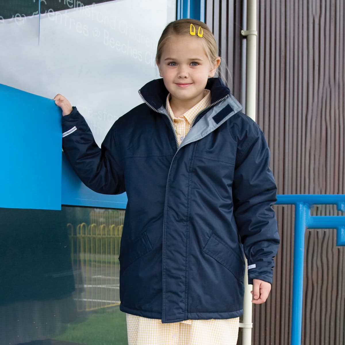 A navy blue Youth Core Winter Parker jacket with reflective detailing, worn by a young girl in a checked dress.