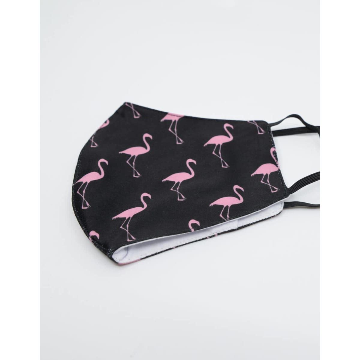 A black face mask with a pink flamingo pattern and an inner label, made of 100% cotton.
