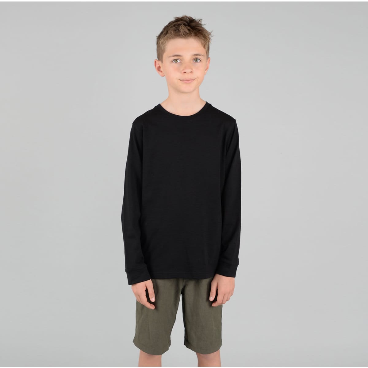 A youth long sleeve tee in black, featuring a simple design and worn by a child, paired with khaki shorts.