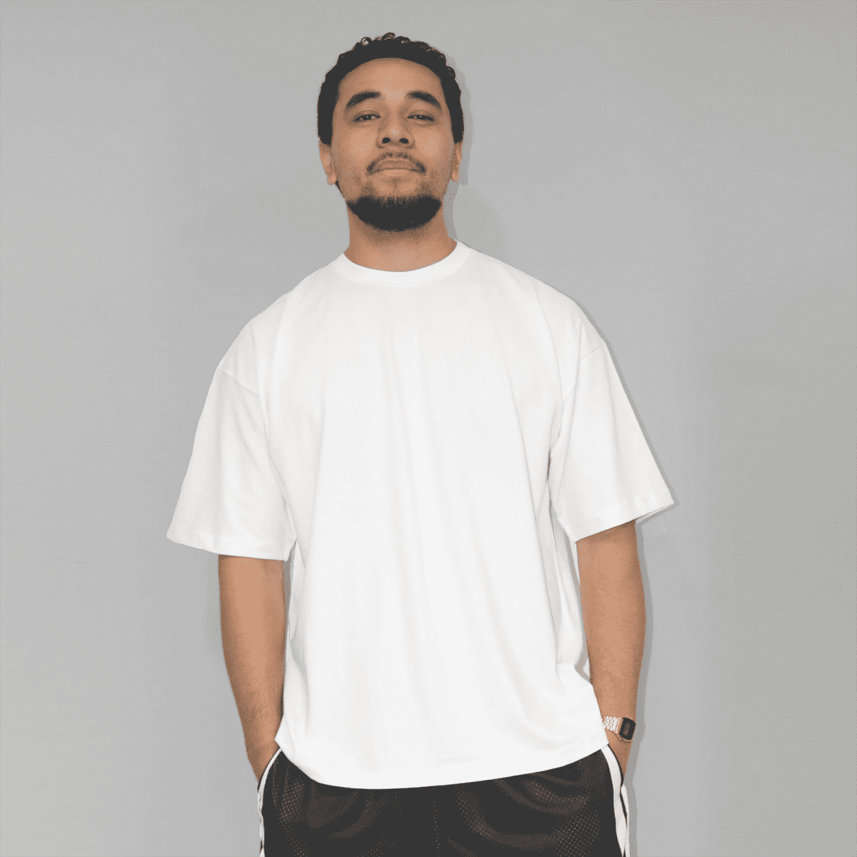 A white oversized T-shirt with short sleeves, featuring a logo on the front. Styled with black shorts.