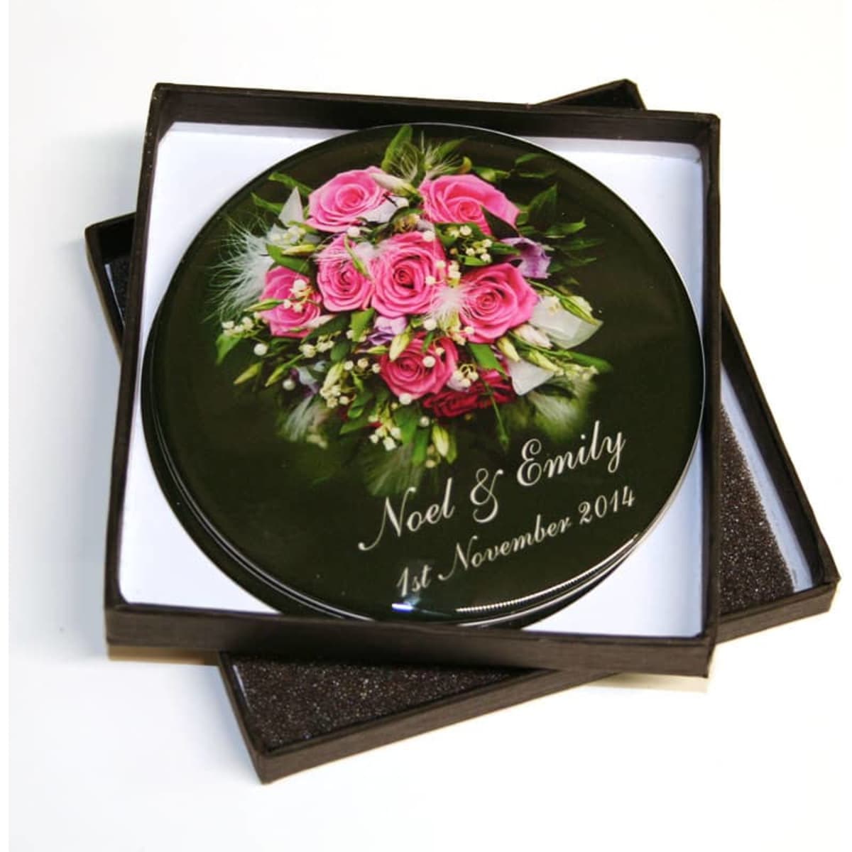 A round, black coaster featuring a floral design with pink roses, presented in a square box.