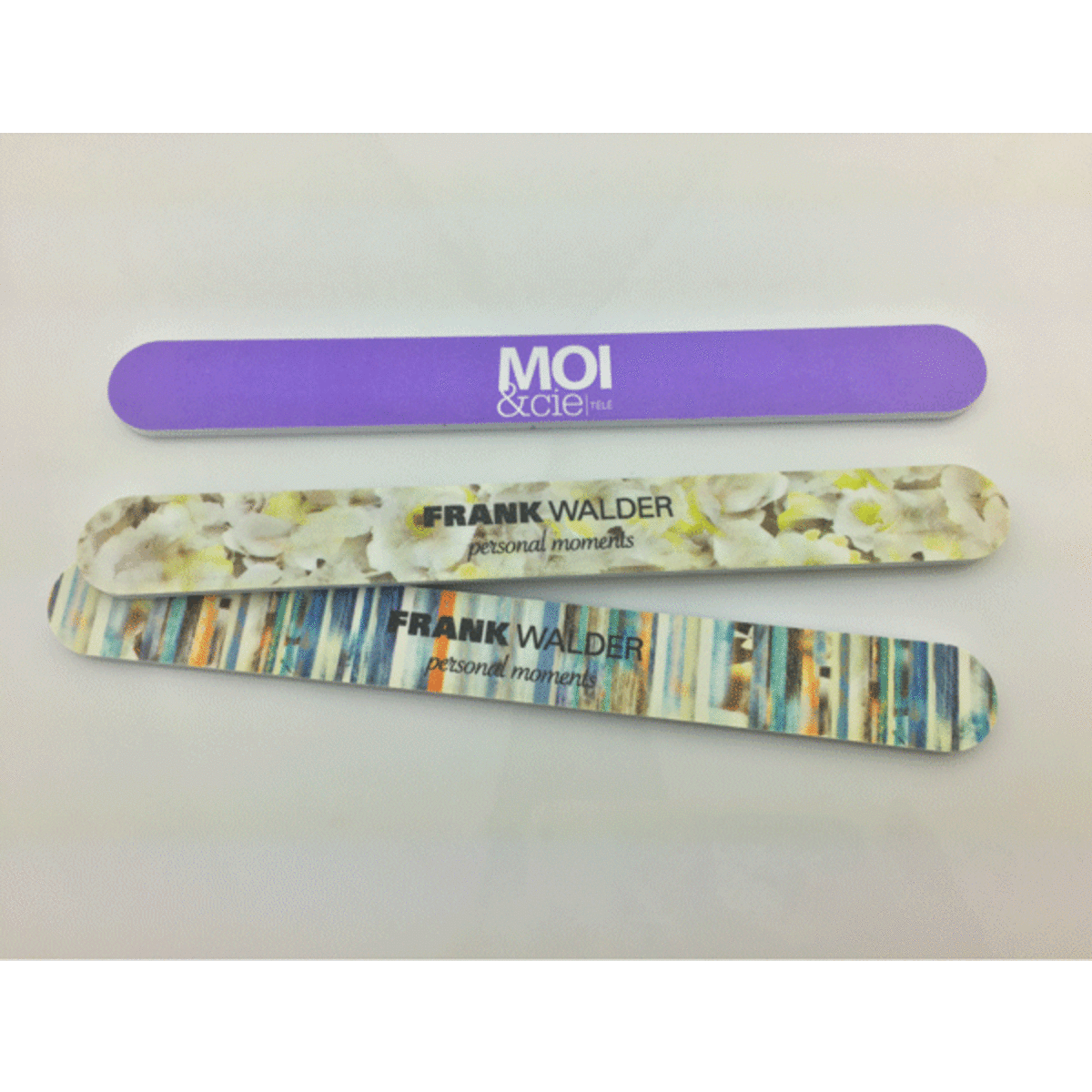 Three emery nail files in varying designs, featuring purple and floral patterns, with branding on two files.