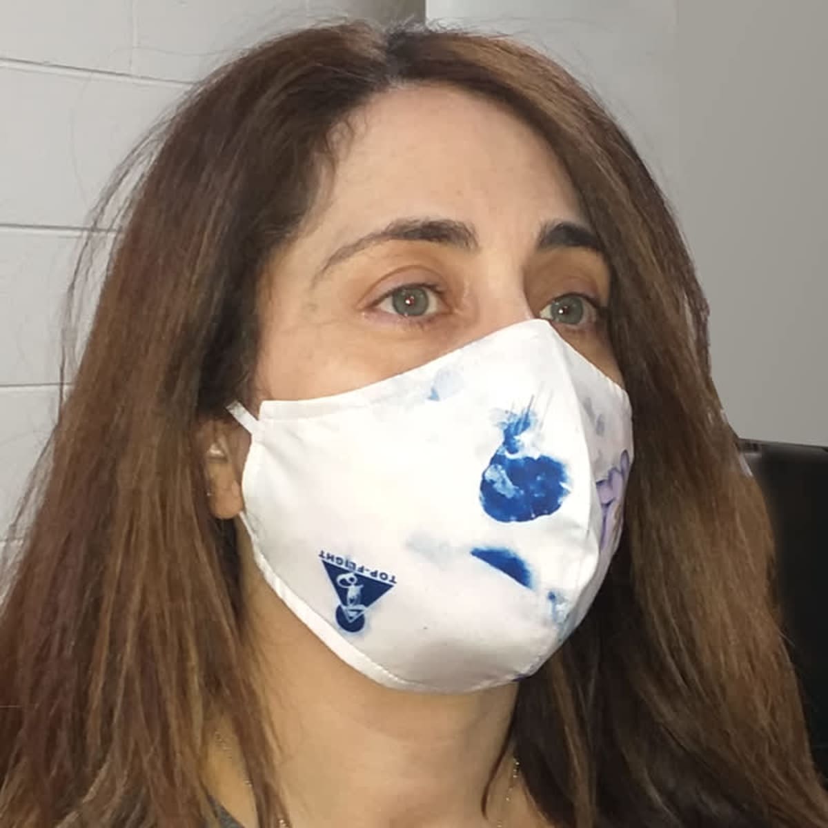 A woman wearing a white face mask with blue patterns and a logo.