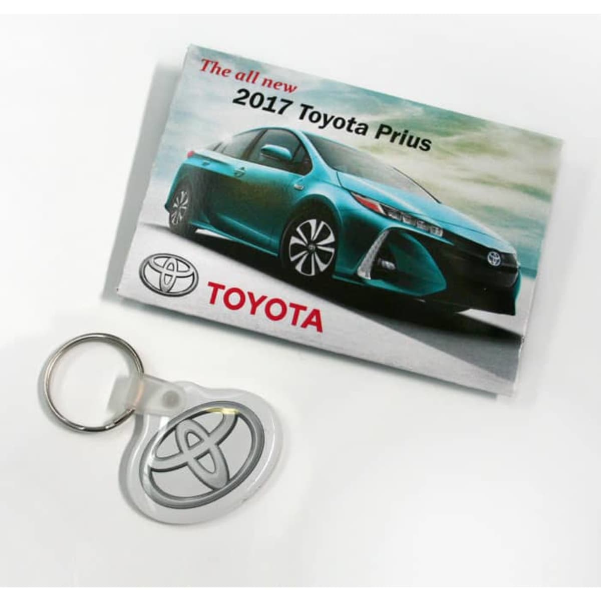 A promotional folder featuring a blue 2017 Toyota Prius and a silver key tag. The folder has a logo.