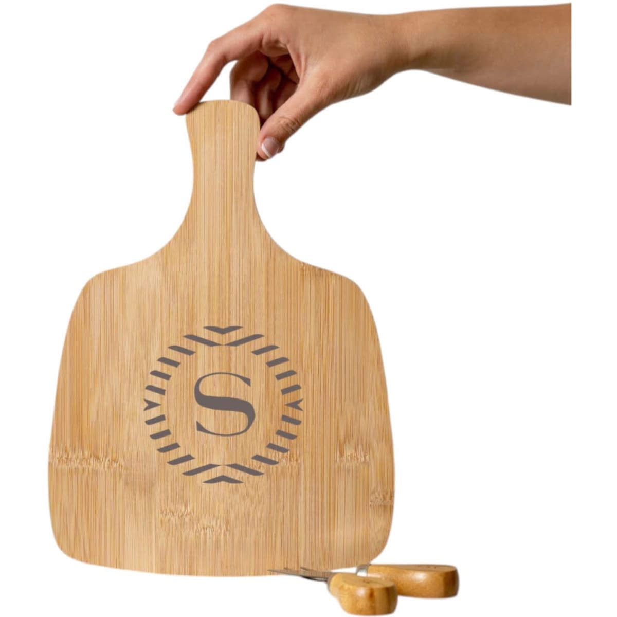 A bamboo cheeseboard with a hand holding it, featuring a decorative design and a knife set below.