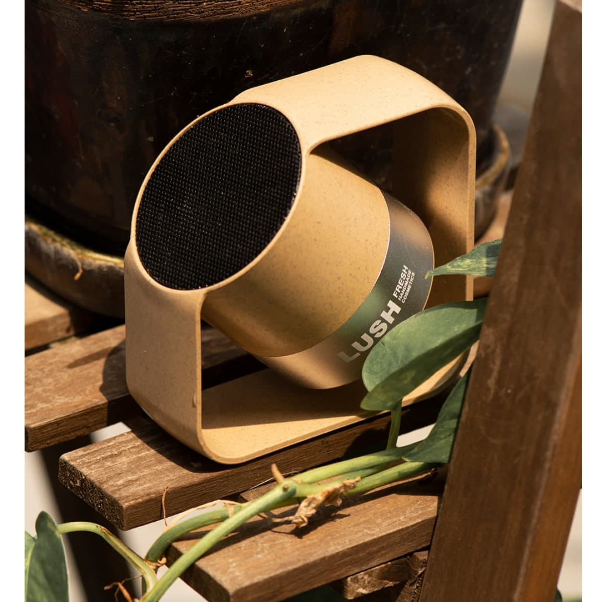 A wireless speaker in a circular design featuring a beige casing and a black speaker grille, set on a wooden surface.