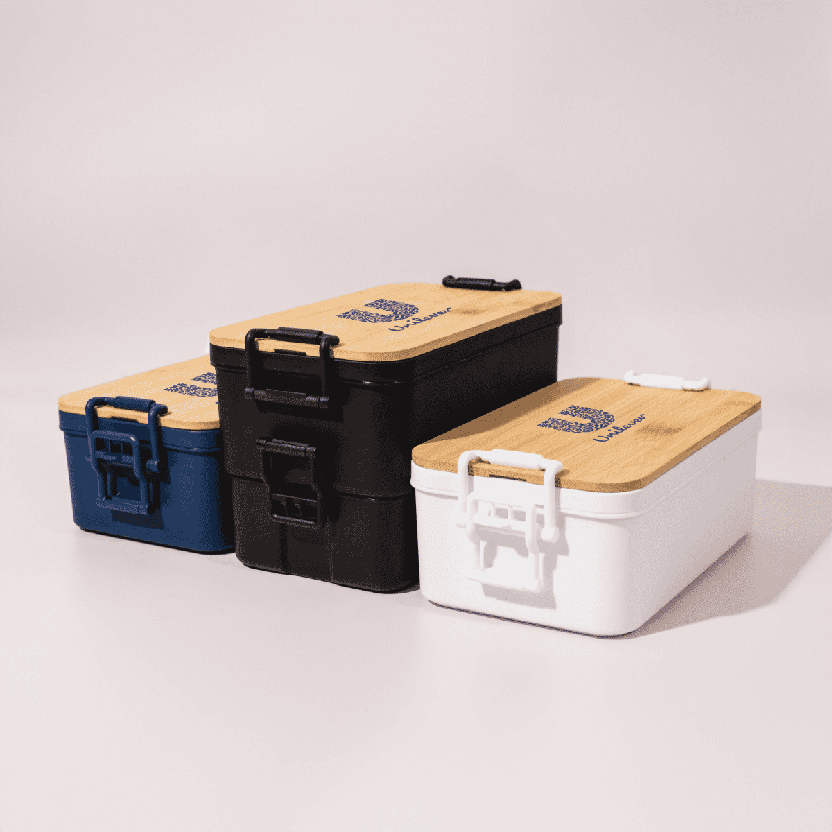 Three stacked lunch boxes in navy blue, black, and white with bamboo lids and a logo on top.