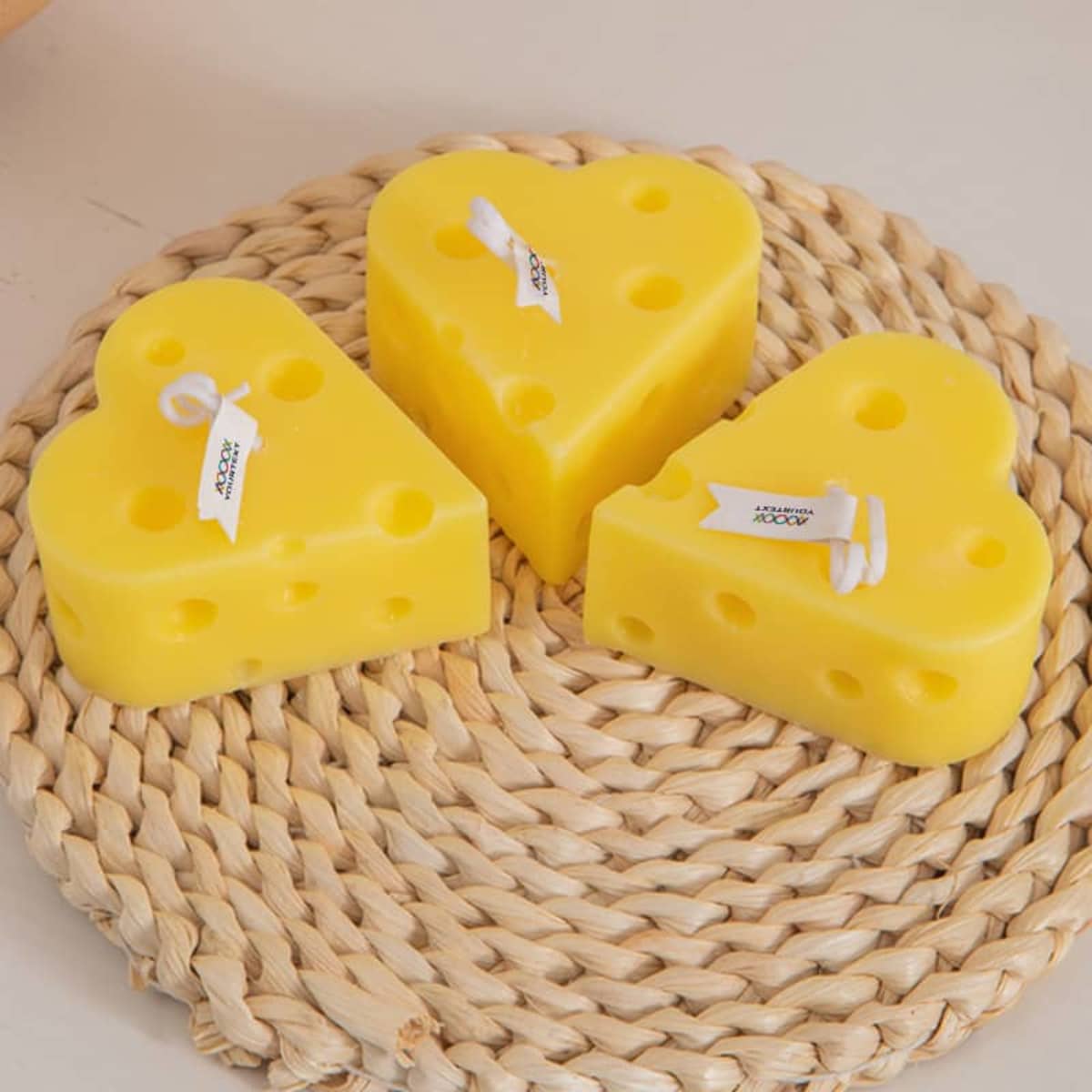 Three heart-shaped candles in bright yellow, designed to resemble cheese, placed on a woven mat.