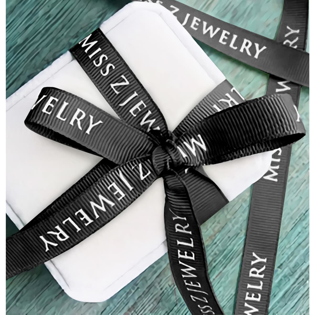 A white gift box wrapped with black ribbed fabric ribbon featuring a logo.