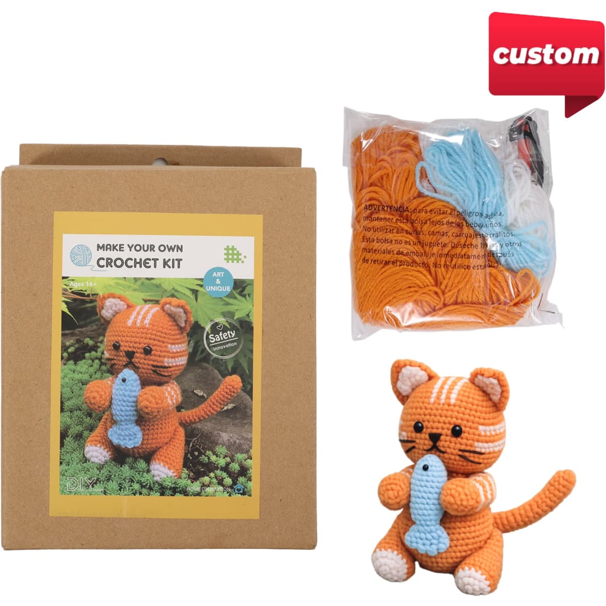 A crochet kit featuring an orange striped kitten with a fish, packaged in a brown box with additional yarn.