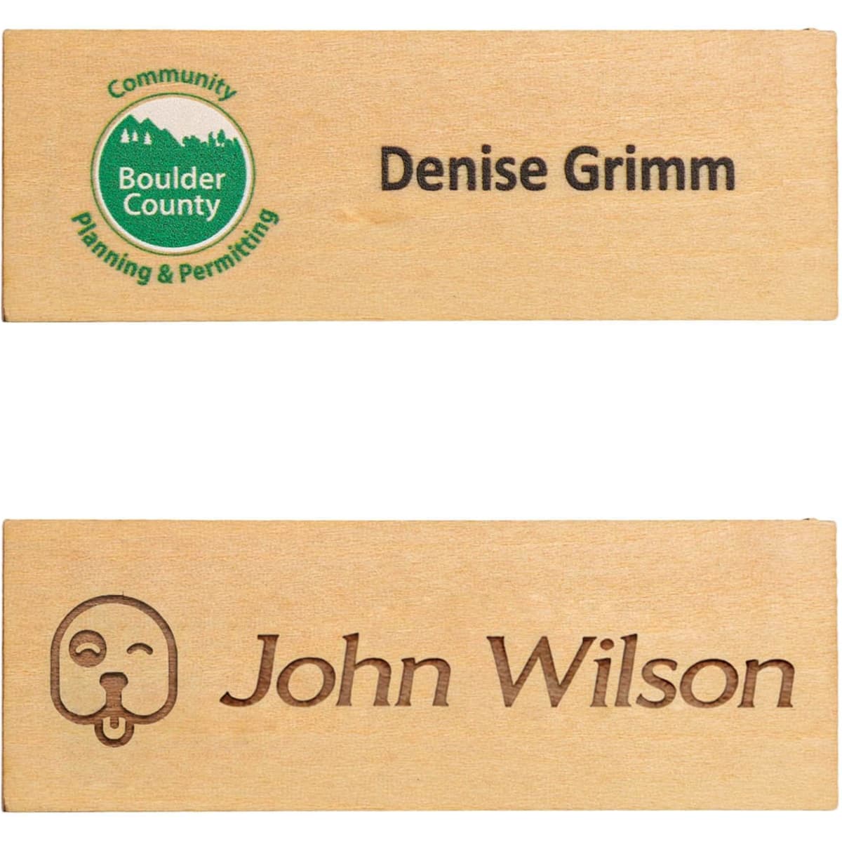 A wooden name badge in light brown with two engraved names and a logo, featuring a simple design.