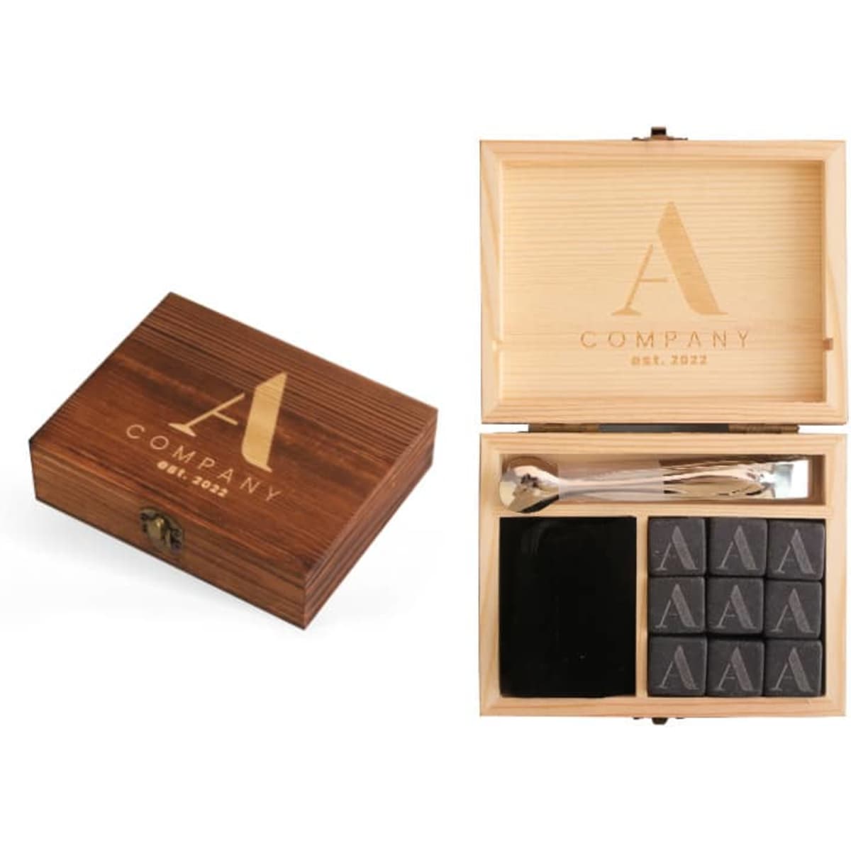 A wooden box featuring a logo, containing nine black whiskey stones and two stirring utensils.