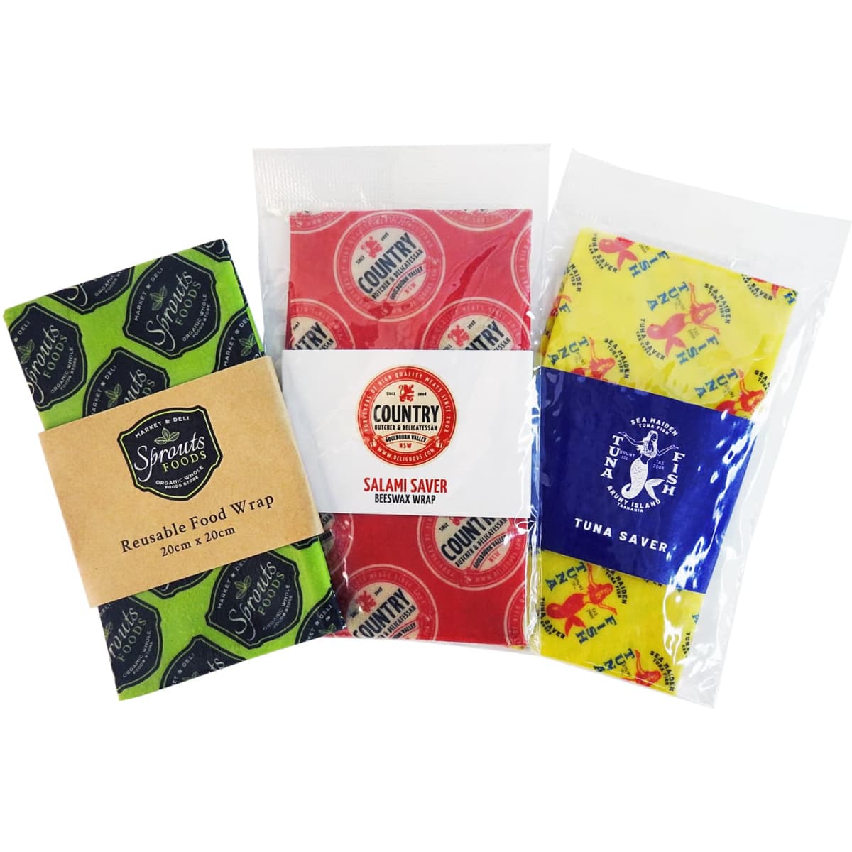 Three beeswax wraps in green, red, and yellow patterns, packaged for reusable food storage. Each features a distinct design and branding.