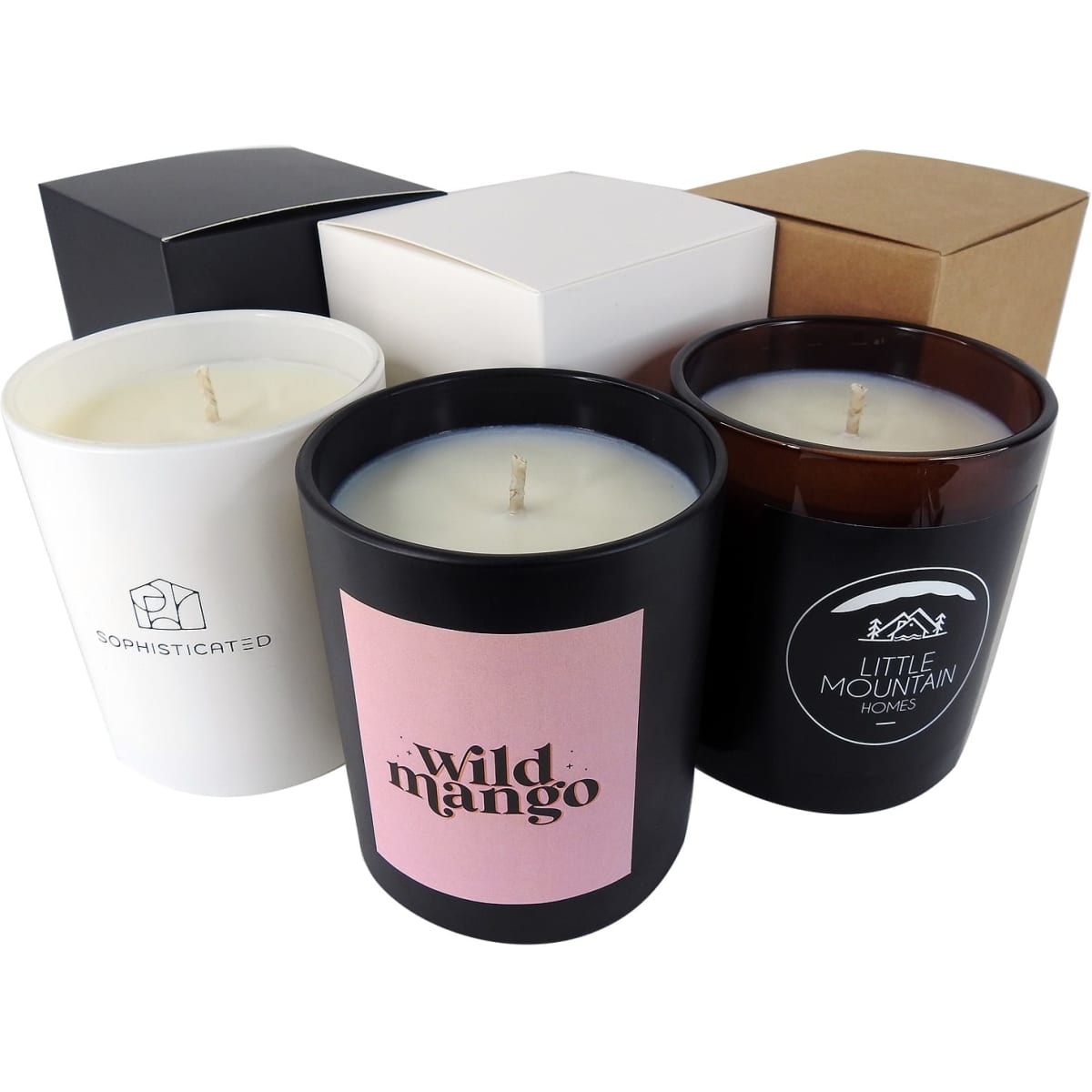 Three candles in various coloured containers: black, white, and brown, with different label designs, beside assorted boxes.