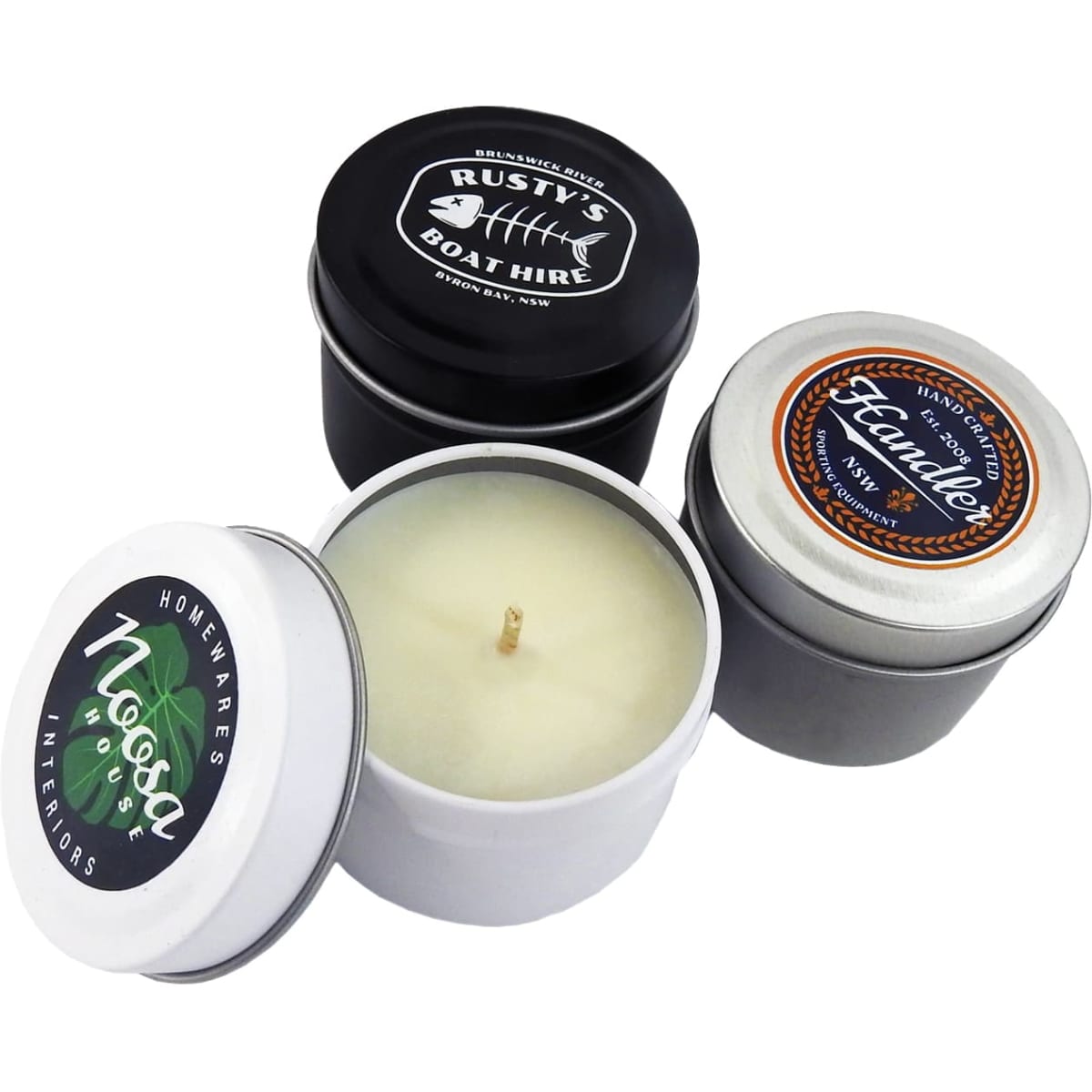 Three small candle tins in black, silver, and white, featuring different designs and a visible wick in the centre of one.