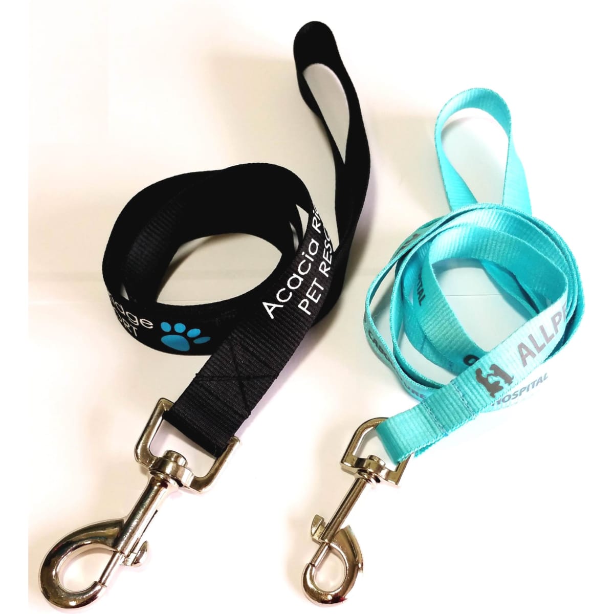 Two dog leads, one black and one light blue, each with a metal clip for attachment. Both feature branding.