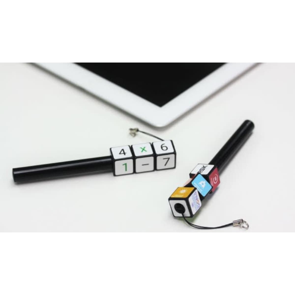 Two black plastic pens with colourful cube designs attached, resting beside a tablet device.