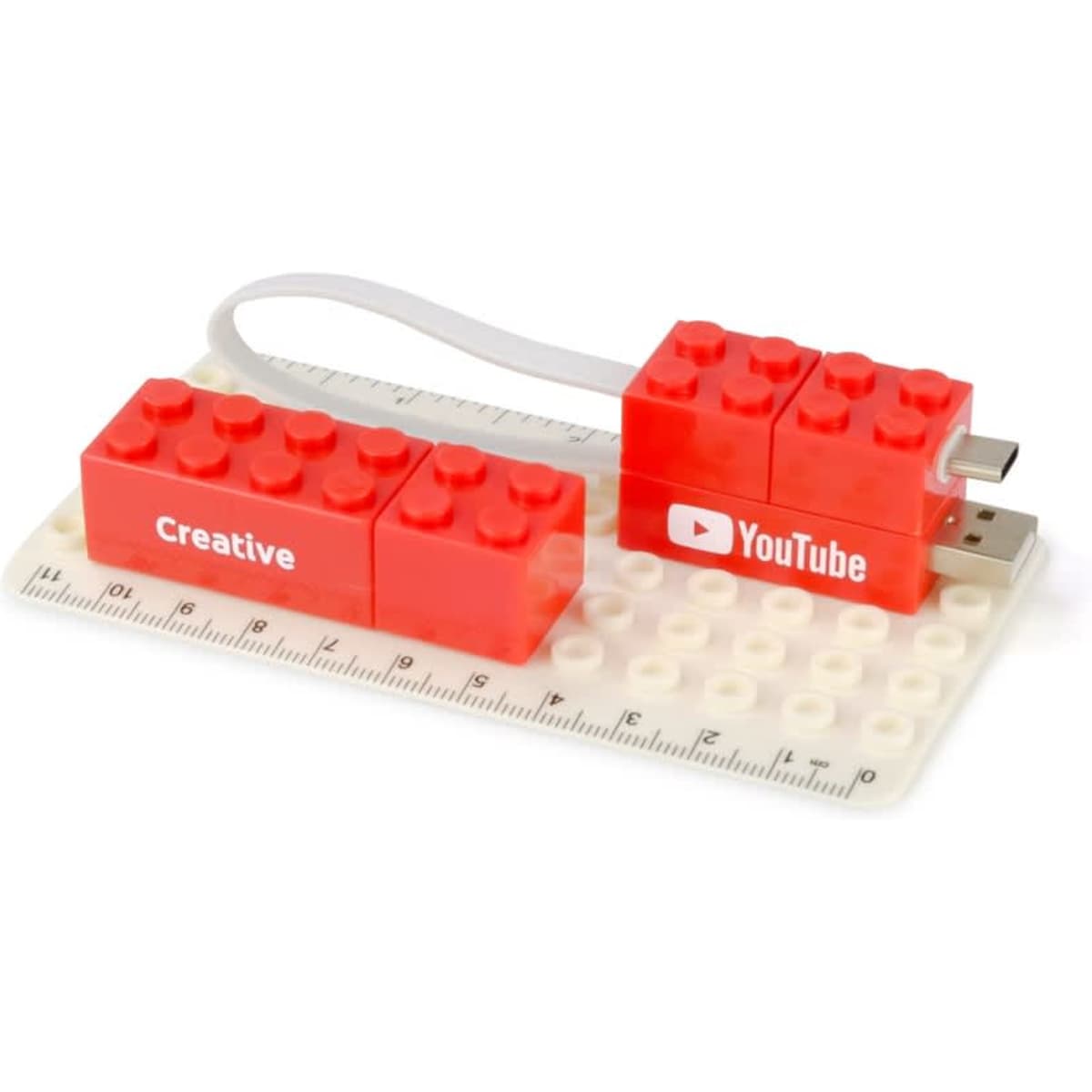 A red USB flash drive designed like Lego blocks, connected to a ruler with a base plate. It features logos and creative text.