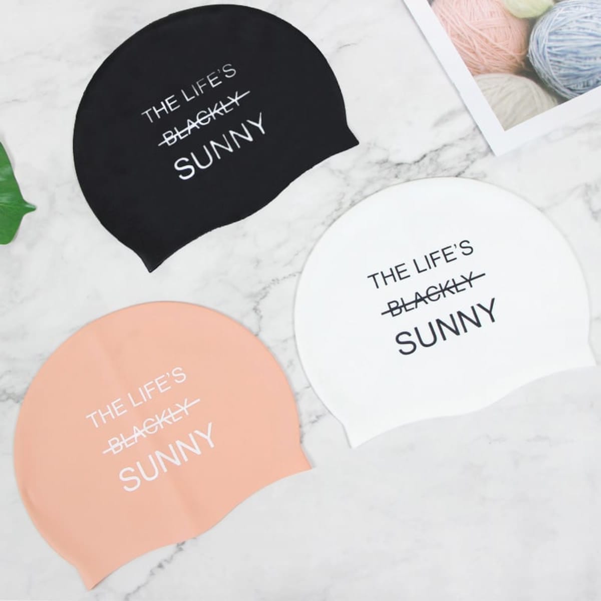 A set of three silicone swim caps in black, white, and peach, featuring a logo on each cap.