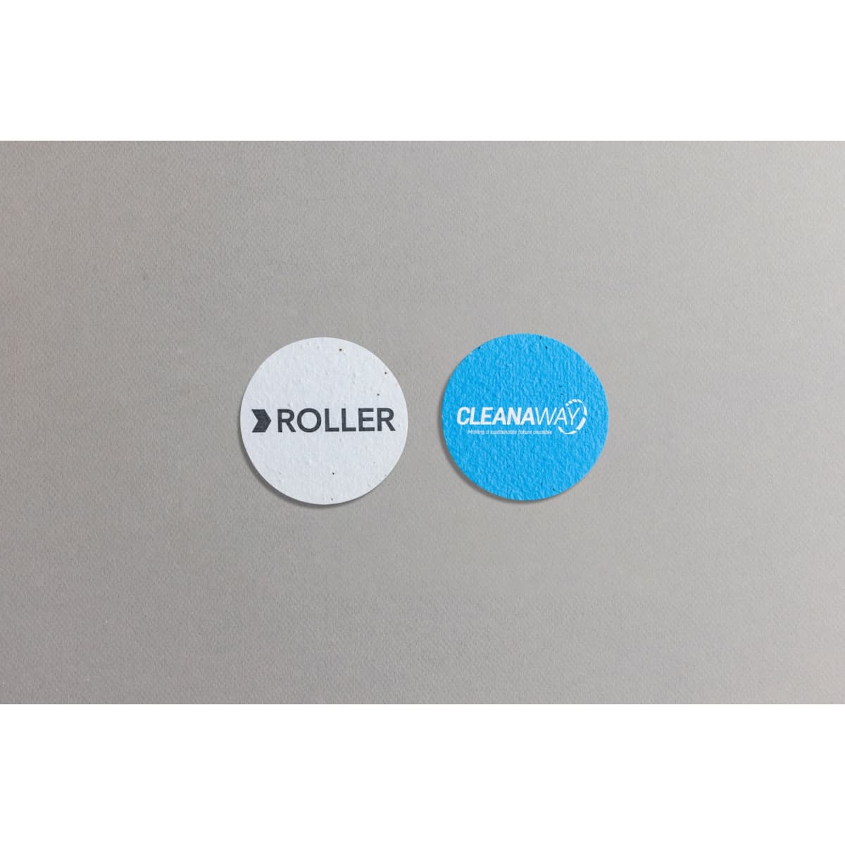 Two circular seed paper pieces, one white with "ROLLER" text and one blue featuring the "CLEANAWAY" logo.