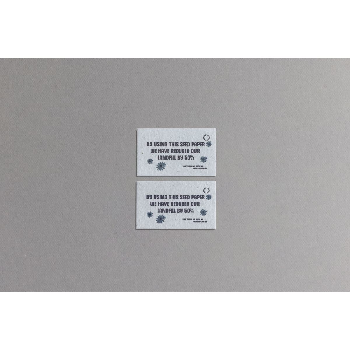 Two rectangular seed paper business cards in light grey with blue text and a circular logo, promoting sustainability.