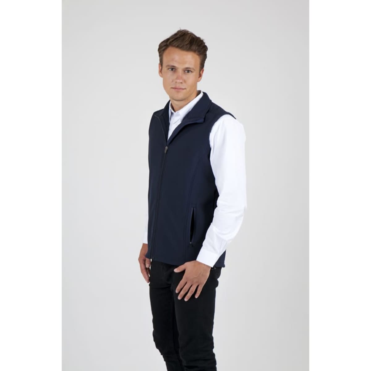 A man wearing a navy blue soft shell vest, standing against a plain background, with a zip and pockets.