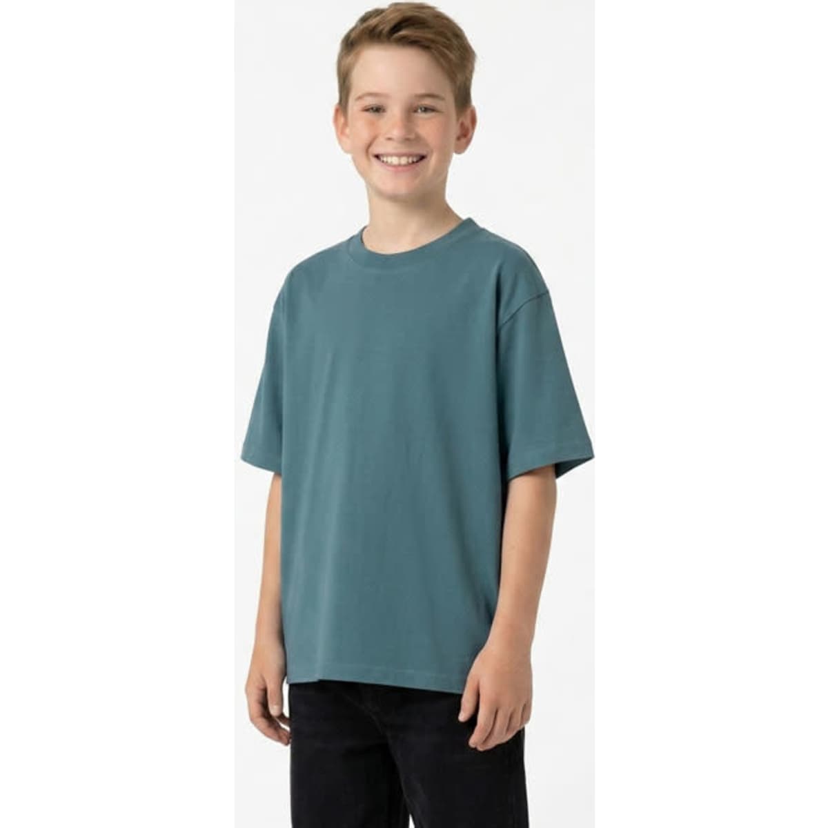 A smiling child wearing a faded teal t-shirt made from 100% organic cotton, paired with dark jeans.