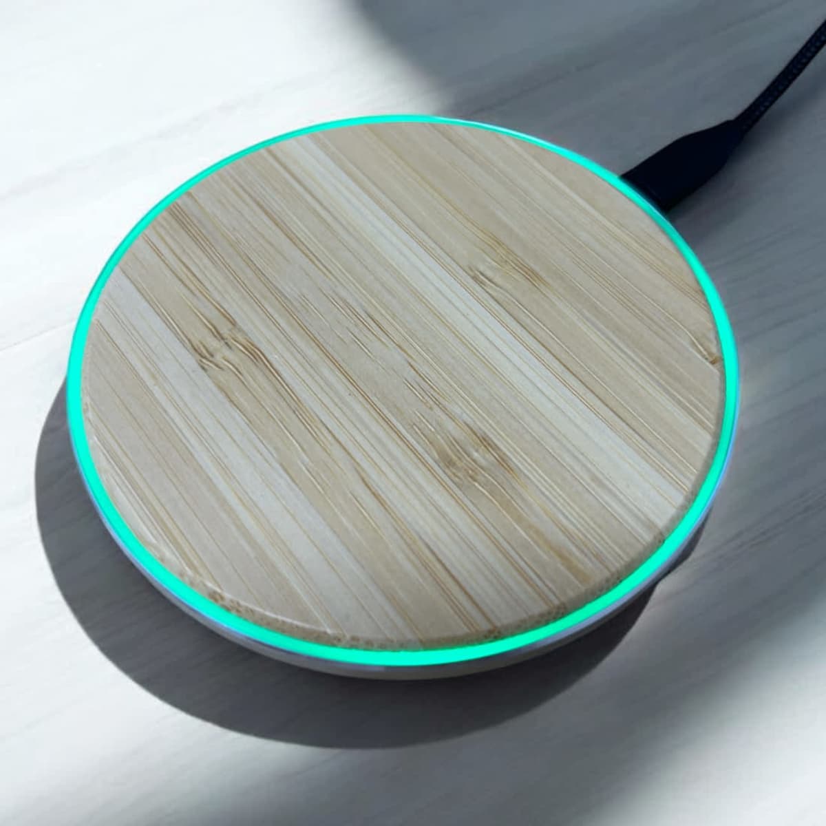 A bamboo wireless charger with a circular design, featuring a glowing blue edge and a black charging cable.