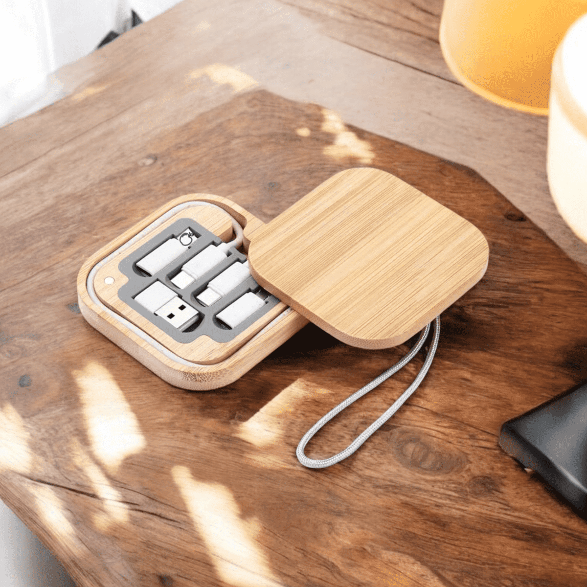 A wooden storage case containing multiple charging and data cables in white, with a grey strap for carrying.