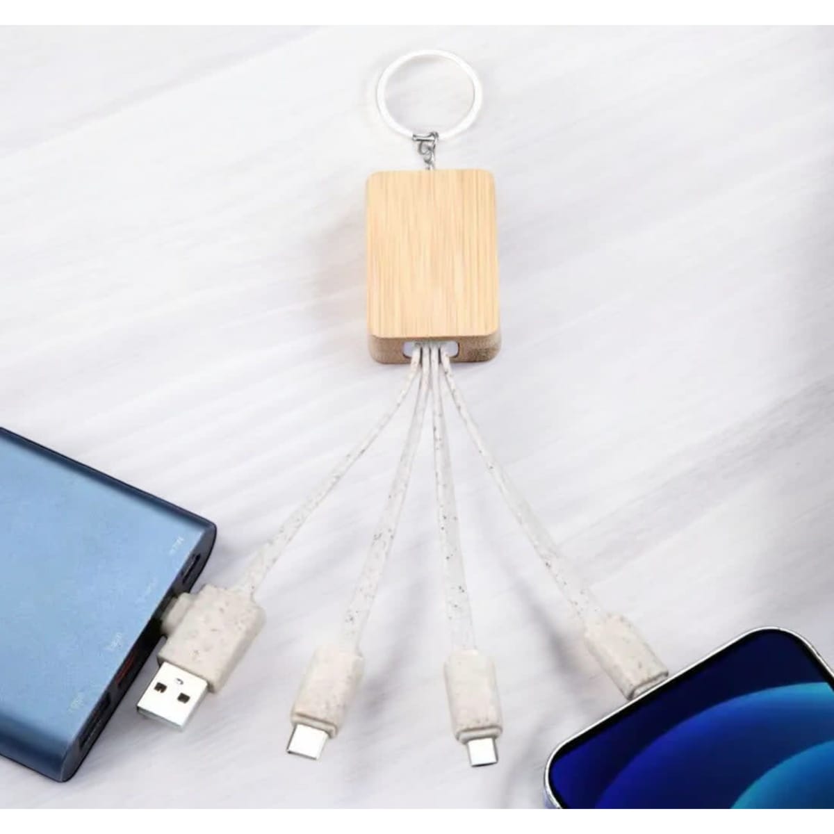 A bamboo multi charger cable with multiple connectors, attached to a keyring, and surrounded by a smartphone and power bank.