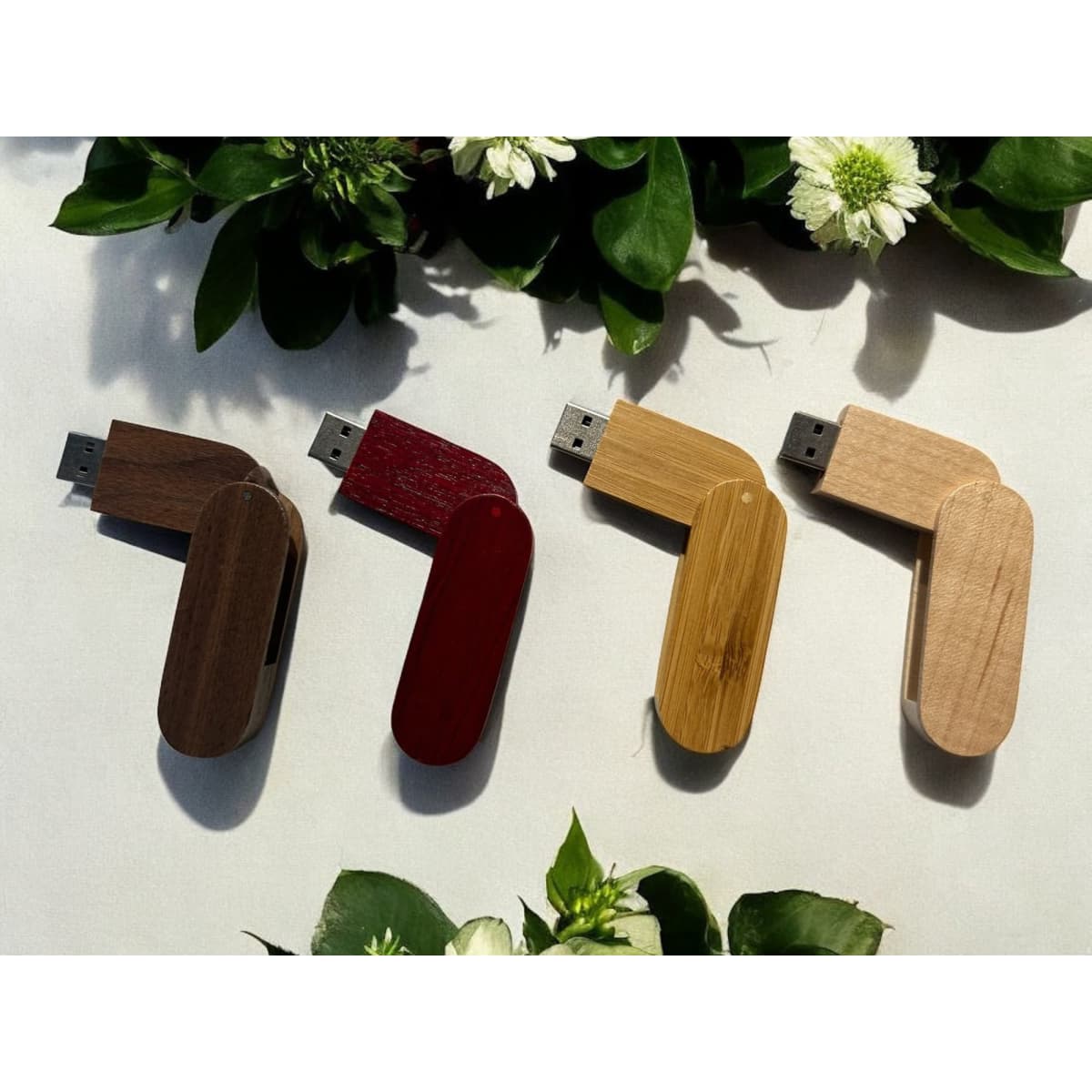 A collection of four wooden swivel flash drives in brown, red, and two shades of light wood, surrounded by greenery.