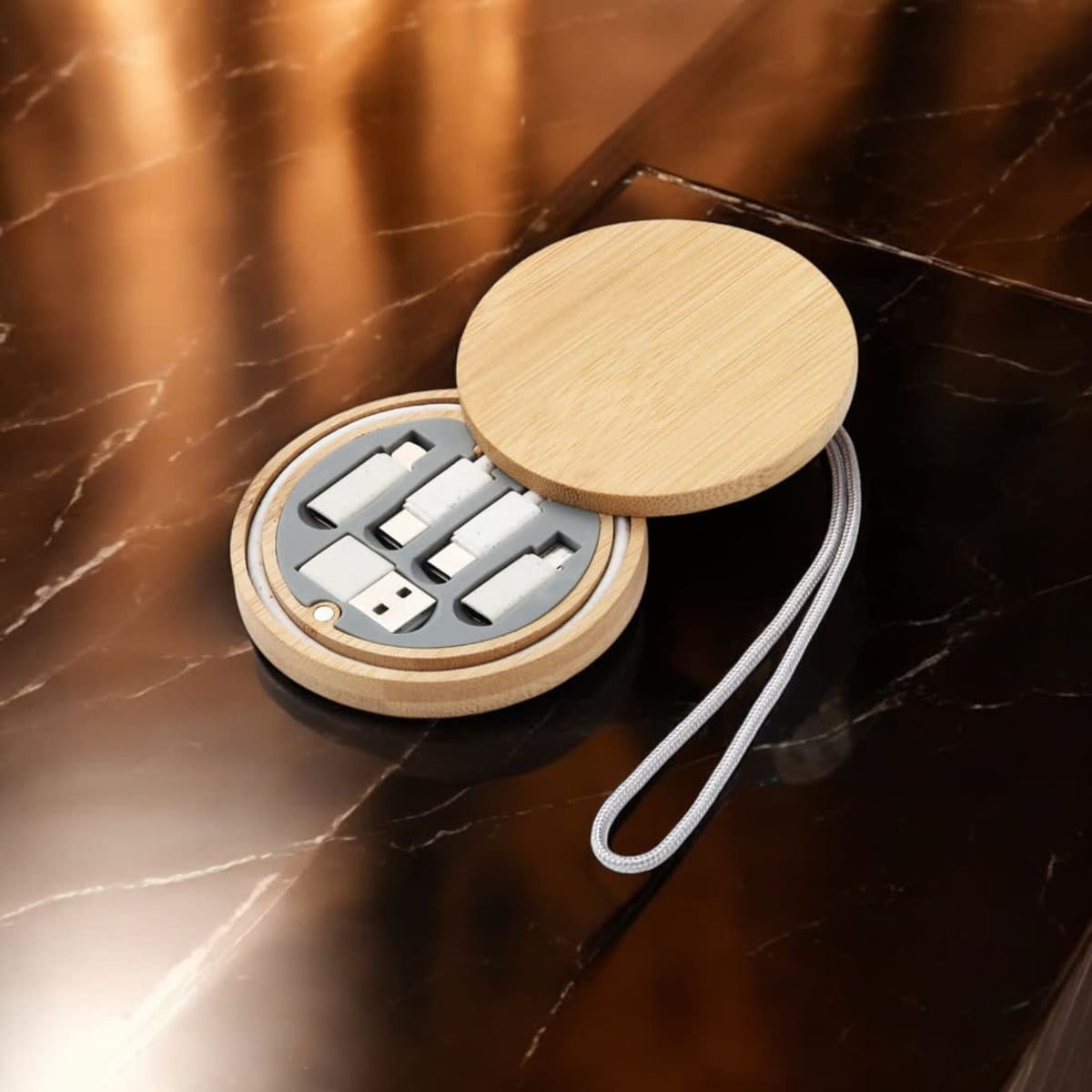 A circular bamboo case containing multiple charging and data cables in grey and silver, with a strap attached.